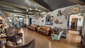 A spacious living area with leather sofas, a coffee table, and a fireplace. A staircase leads to an upper level, and a Christmas tree is visible.