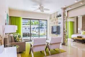 Una habitación de hotel moderna con balcón, televisor de pantalla plana, sofá y zona de comedor con sillas.