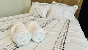 Una cama bien tendida con sábanas blancas y una colcha estampada, dos toallas enrolladas sobre la cama y un cabecero de madera.