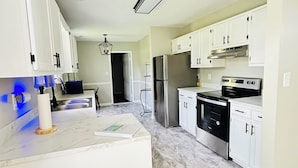 Una cocina moderna con armarios blancos, una isla central, electrodomésticos de acero inoxidable y suelo de mármol.