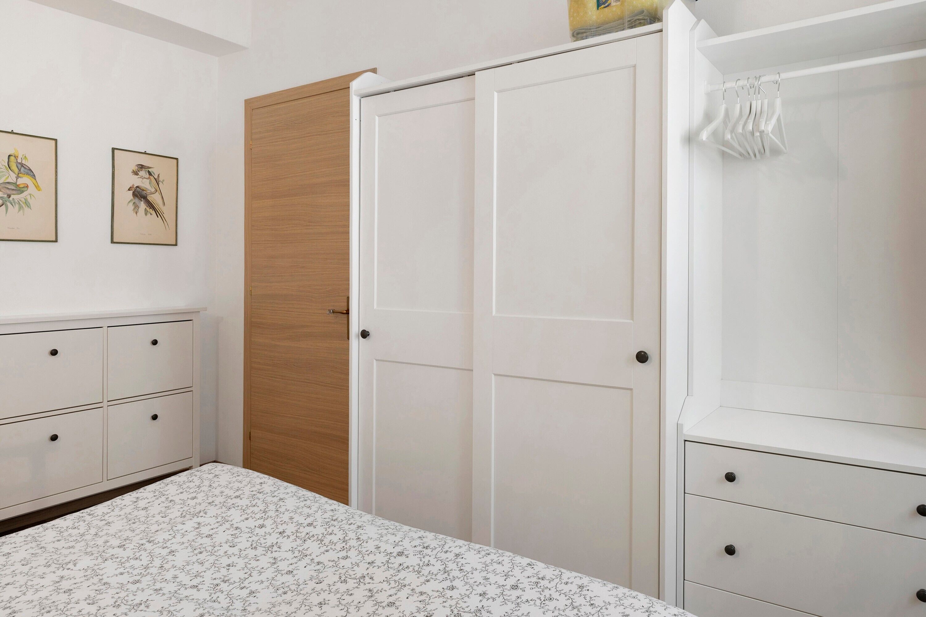 Un dormitorio con cama, armario, puerta de madera y dos cuadros en la pared.