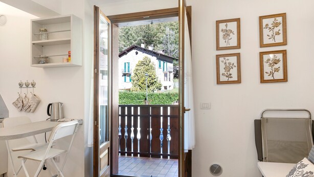 Quarto pequeno com área de refeições, uma cama e vista para uma casa através de uma porta.