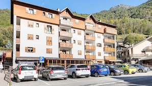 Um edifício com várias andares, varandas, área de estacionamento e montanhas ao fundo.
