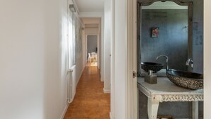 Een gang met een witte deur, een spiegel en een wastafel met twee bakken.