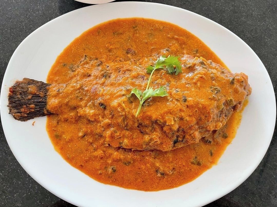 Un plato blanco con pescado cubierto en salsa roja, adornado con una hoja.