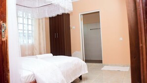 A bedroom with a bed, a wardrobe, and a bathroom door. - Jafra Elephant Inn (Eldoret)