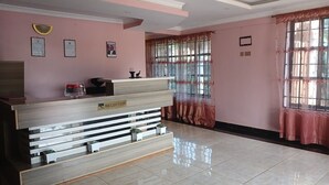 A reception area with a wooden reception desk, a nameplate, framed certificates, and a window with curtains. - Jafra Elephant Inn (Eldoret)