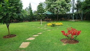 A well-maintained garden with a stone pathway, green grass, and a variety of plants including red flowers. - Jafra Elephant Inn (Eldoret)