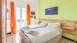 A double bed with white linens, a wooden headboard, and a view of the outdoors through a window with orange curtains. - Room 'Stanza 1' with Sea View, Shared Terrace and Wi-Fi (Castiglione Chiavarese)