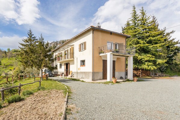 A two-story house with a balcony, a gravel driveway, and surrounding greenery.
