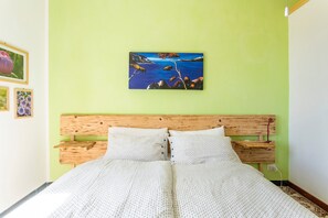 A bed with a wooden headboard, a green wall, and a framed painting above it.