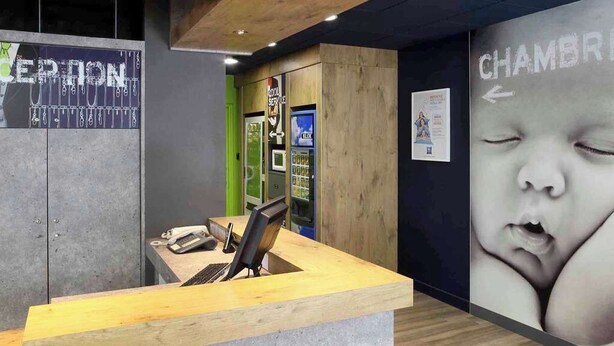Un mostrador de recepción con encimera de madera y una computadora. Se observa una pared con un cartel grande y un letrero que dice "CHAMBR".