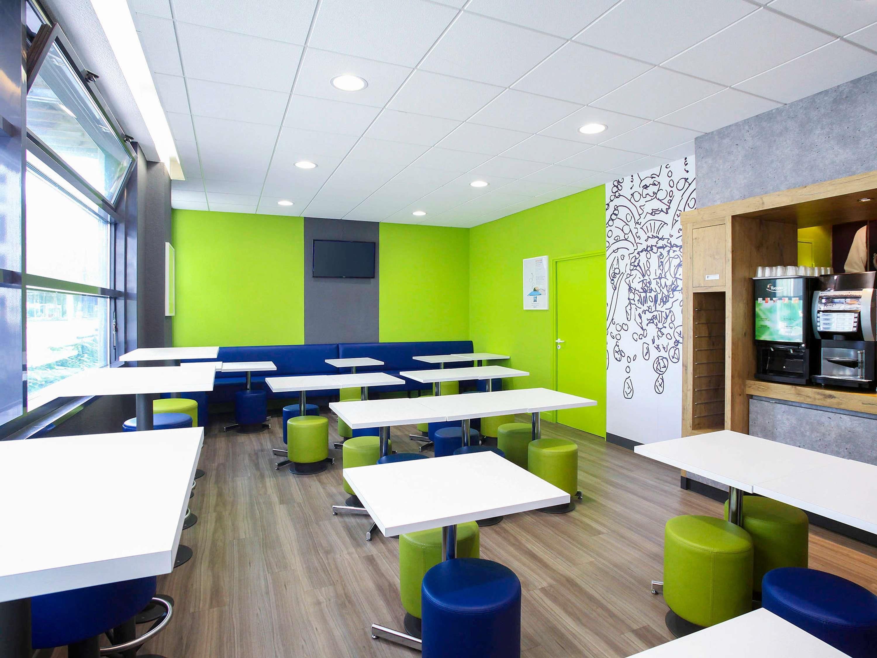 A modern cafe interior with multiple tables and green and blue seating.