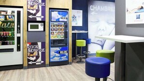 Un área de quioscos moderna con una máquina de autoservicio KIX, una máquina expendedora y un letrero que dice 'Cool Service'.