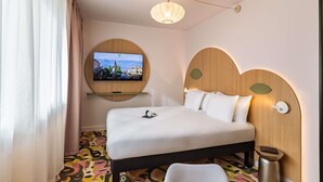 A hotel room with a bed, a television mounted on the wall, a bedside table, and a unique patterned carpet. - ibis Styles Metz Centre (Ouverture Janvier 2026) (Metz)