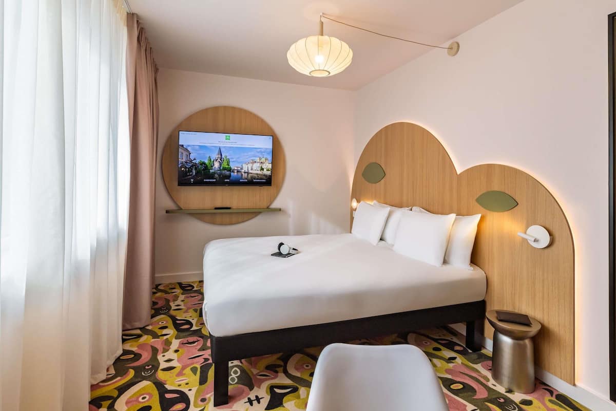 A hotel room with a bed, a television mounted on the wall, a bedside table, and a unique patterned carpet.