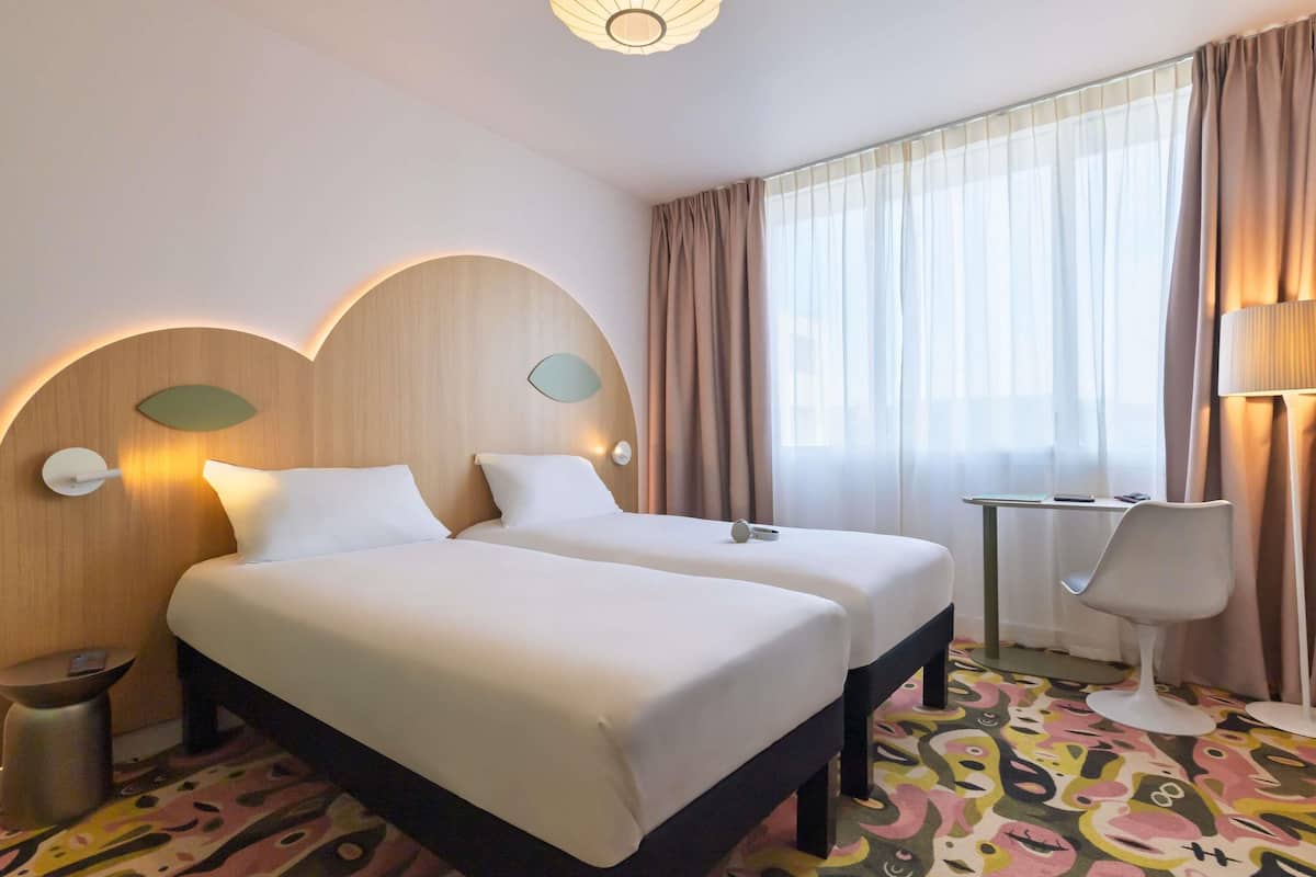 A hotel room with two beds, a desk, a chair, a lamp, and a patterned carpet.