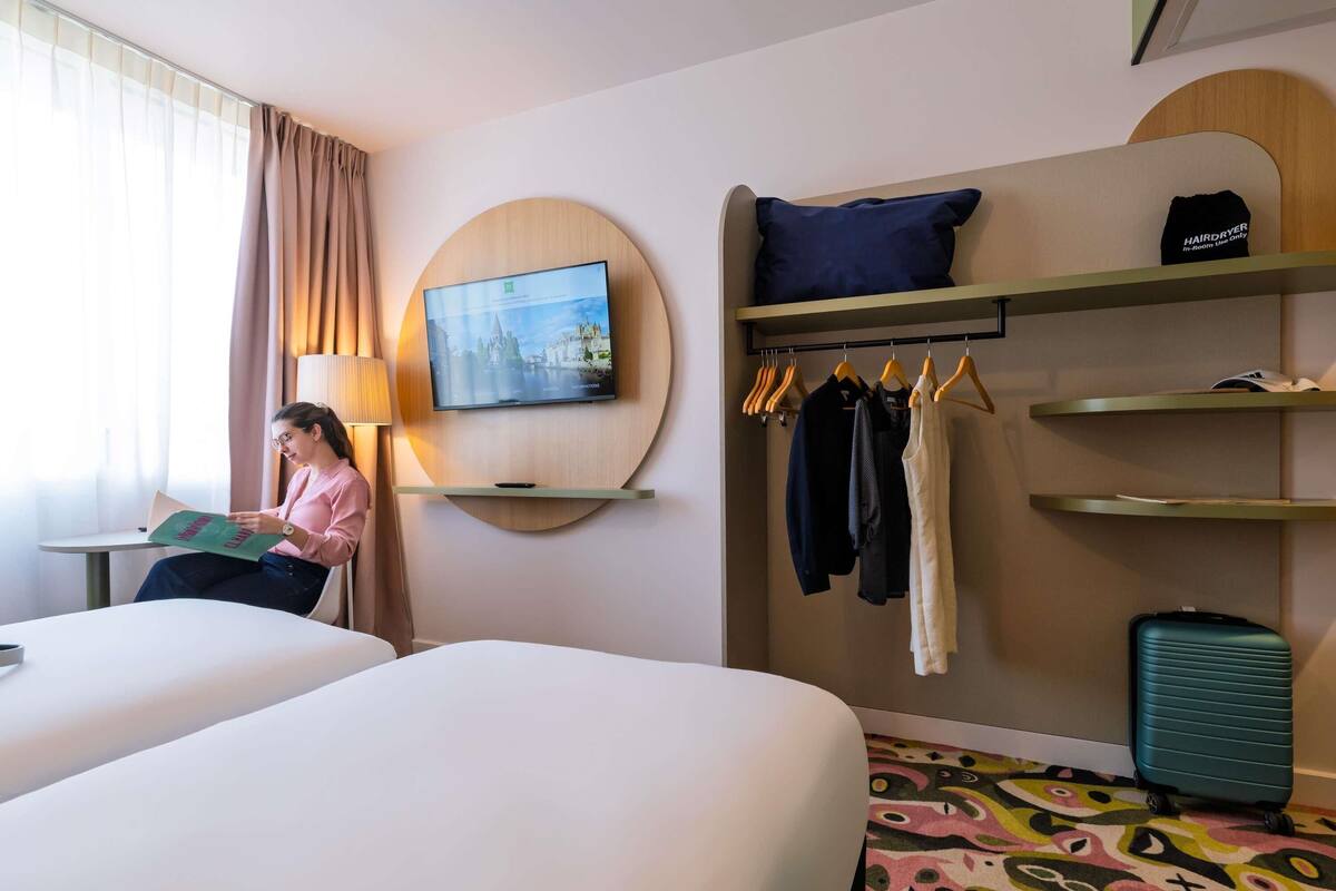 A hotel room with two beds, a TV mounted on the wall, a clothing rack, and a suitcase.