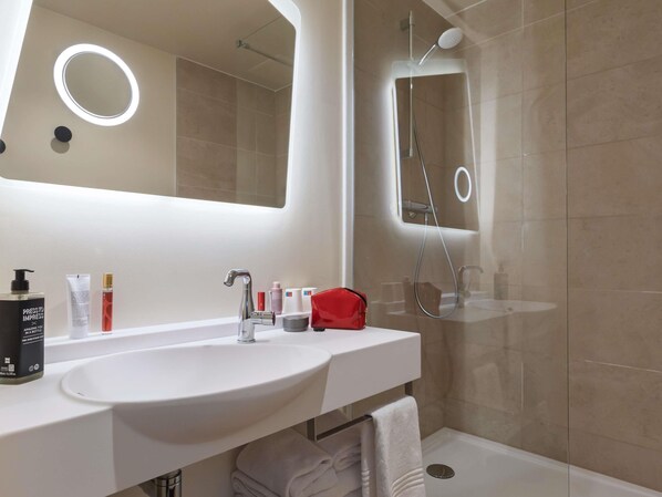 Un baño moderno con un lavamanos blanco, un espejo y una ducha.