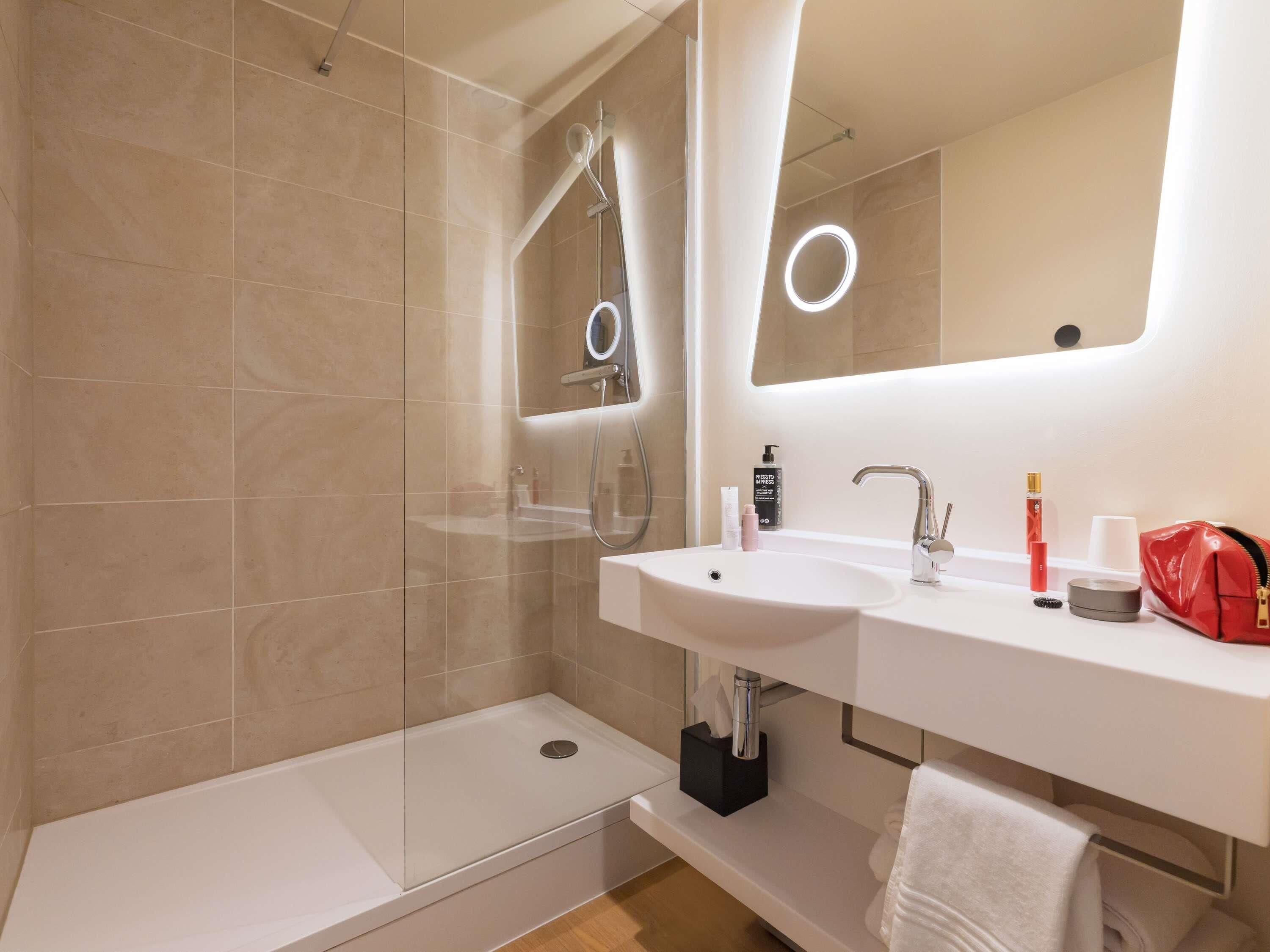 A modern bathroom with a glass-enclosed shower, a double sink vanity, and a large mirror with integrated lighting.