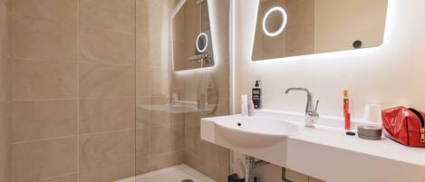 A modern bathroom with a glass-enclosed shower, a double sink vanity, and a large mirror with integrated lighting.