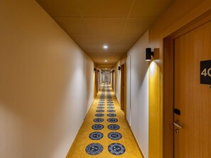 Un couloir dâhĂŽtel avec un tapis Ă motifs, des portes en bois et un panneau indiquant le numĂ©ro de la chambre sur le mur.
