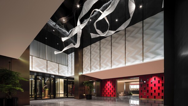 A spacious lobby with a reflective floor, a large abstract light installation, and a red patterned wall. - Mercure Beijing The Grand Canal Cbd (Tongzhou)