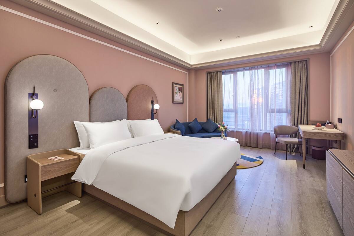 Ett hotellrum med en stor säng, ett skrivbord, en stol och utsikt över staden genom fönstret.