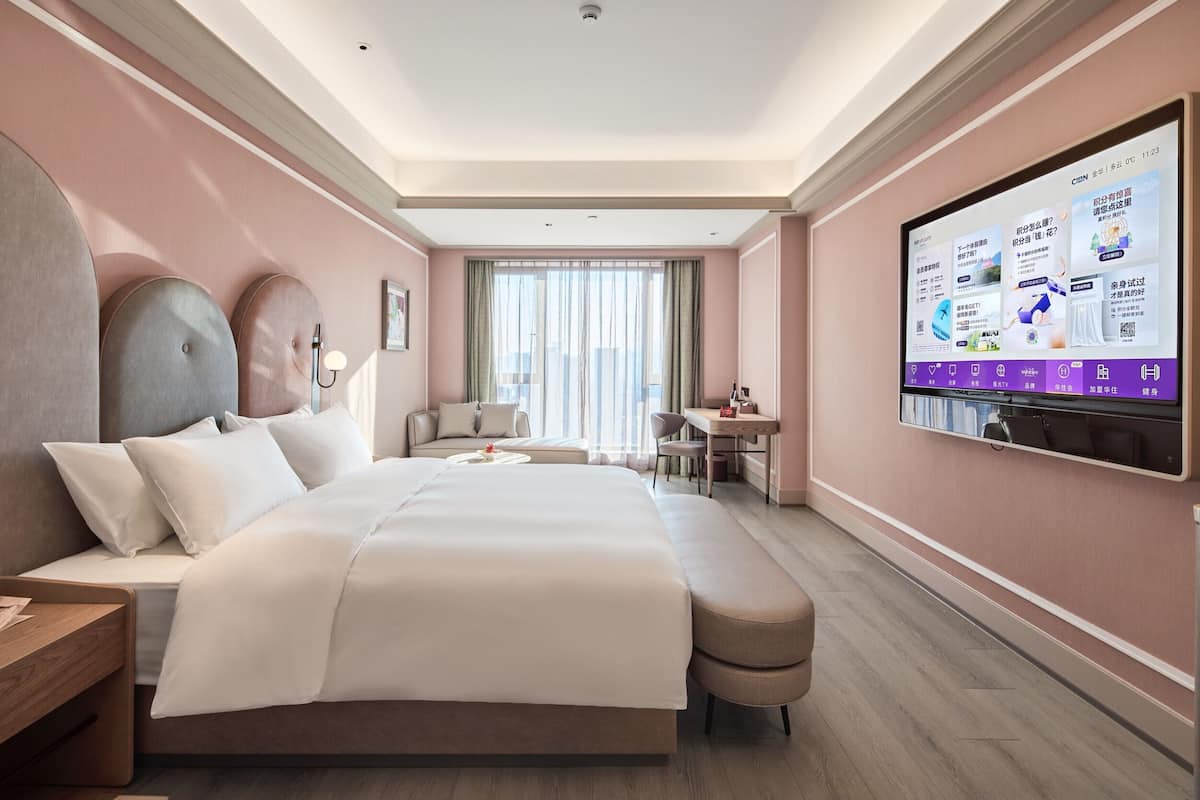 Ett modernt hotellrum med en stor säng, ett skrivbord, en stol och en tv som är monterad på väggen.