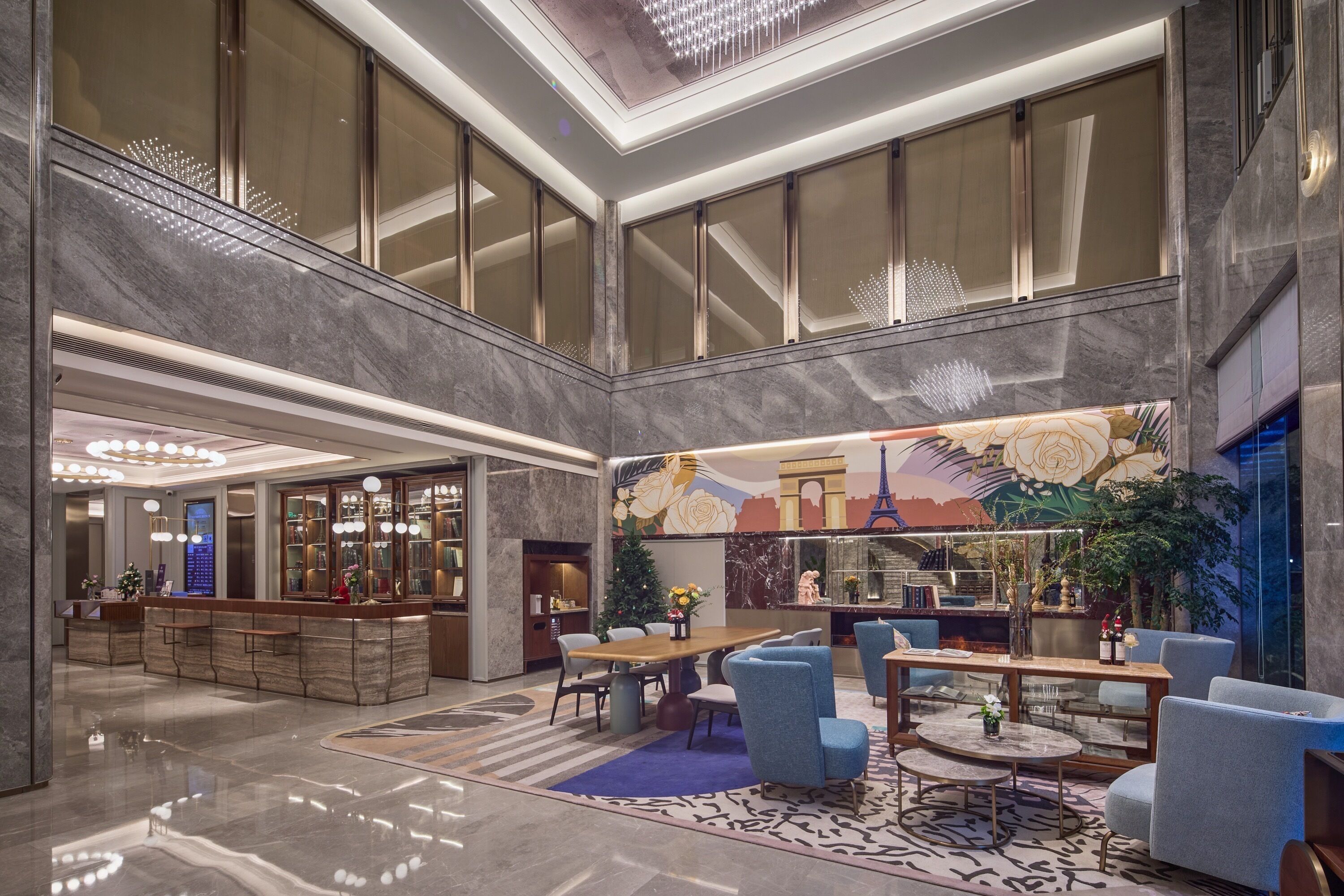 Eine geräumige Lobby mit hoher Decke, einem Empfangsbereich, Sitzbereichen und einem dekorativen Wandgemälde.