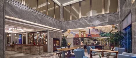 A spacious lobby with a high ceiling, a reception desk, seating areas, and a decorative mural.