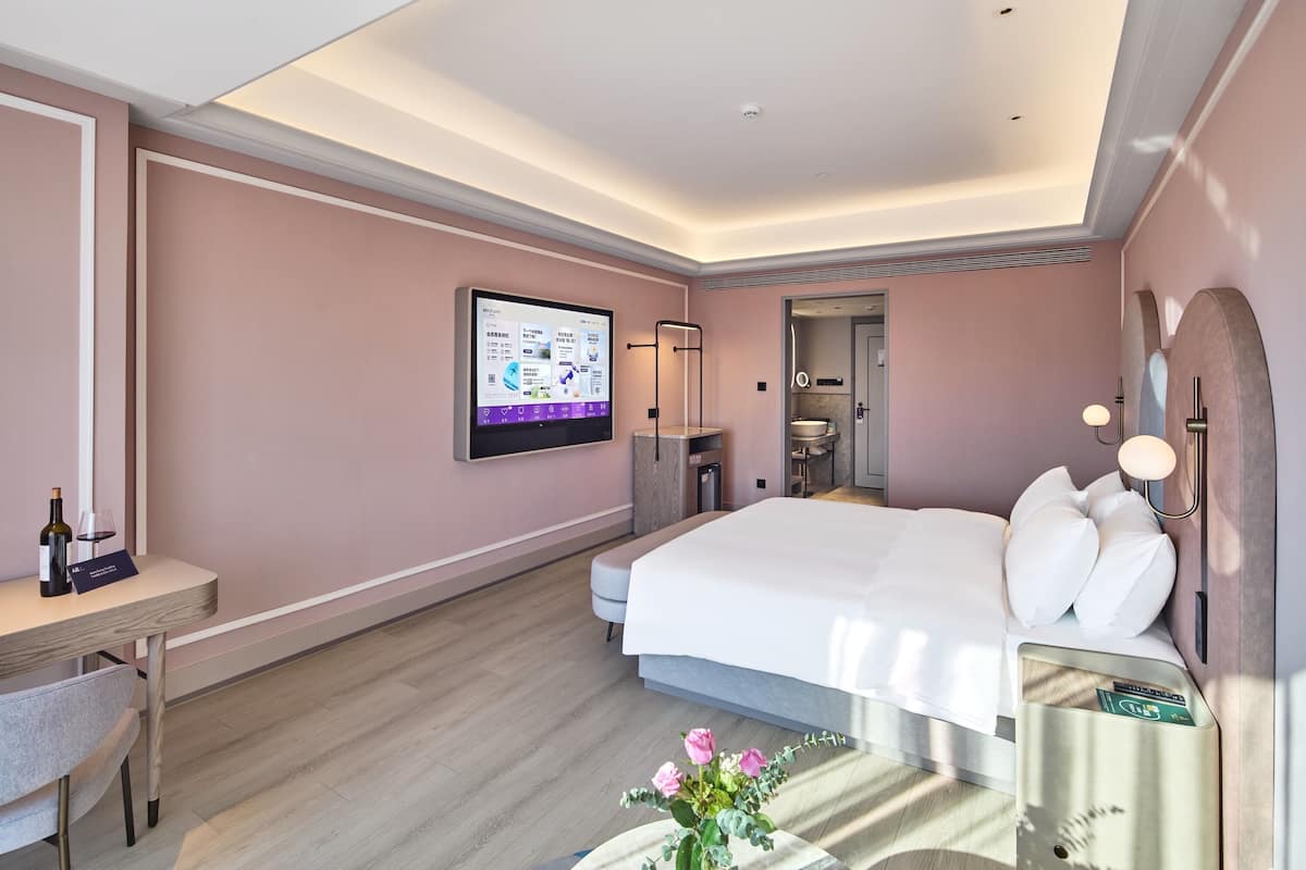 Ett modernt hotellrum med en stor säng, ett skrivbord, en platt-TV och ett badrum som syns genom en öppen dörr.