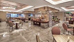Een ruime hotellobby met marmeren vloer, meerdere zithoeken en een centraal gelegen bar voorzien van diverse voorzieningen.