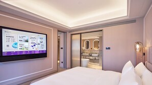 Een moderne hotelkamer met een groot bed, een televisie aan de muur, een badkamer met wastafel en spiegel, en een inbouw plafondlamp.