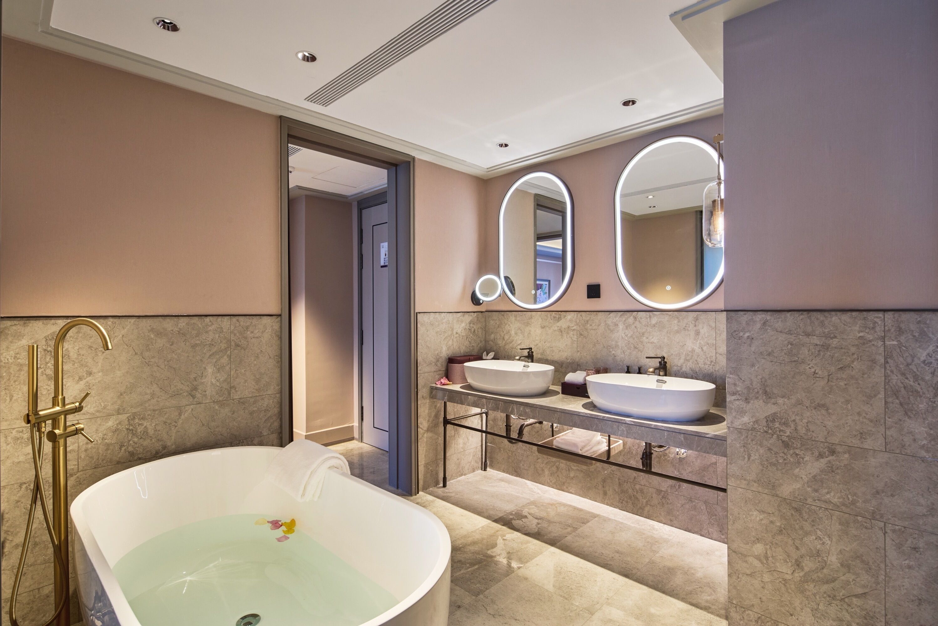 A modern bathroom with a freestanding bathtub, two sinks, and a large mirror with lights.
