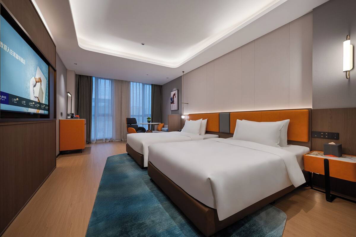 Une chambre d’hôtel moderne avec deux lits, une télévision, un bureau et une vue sur la ville.