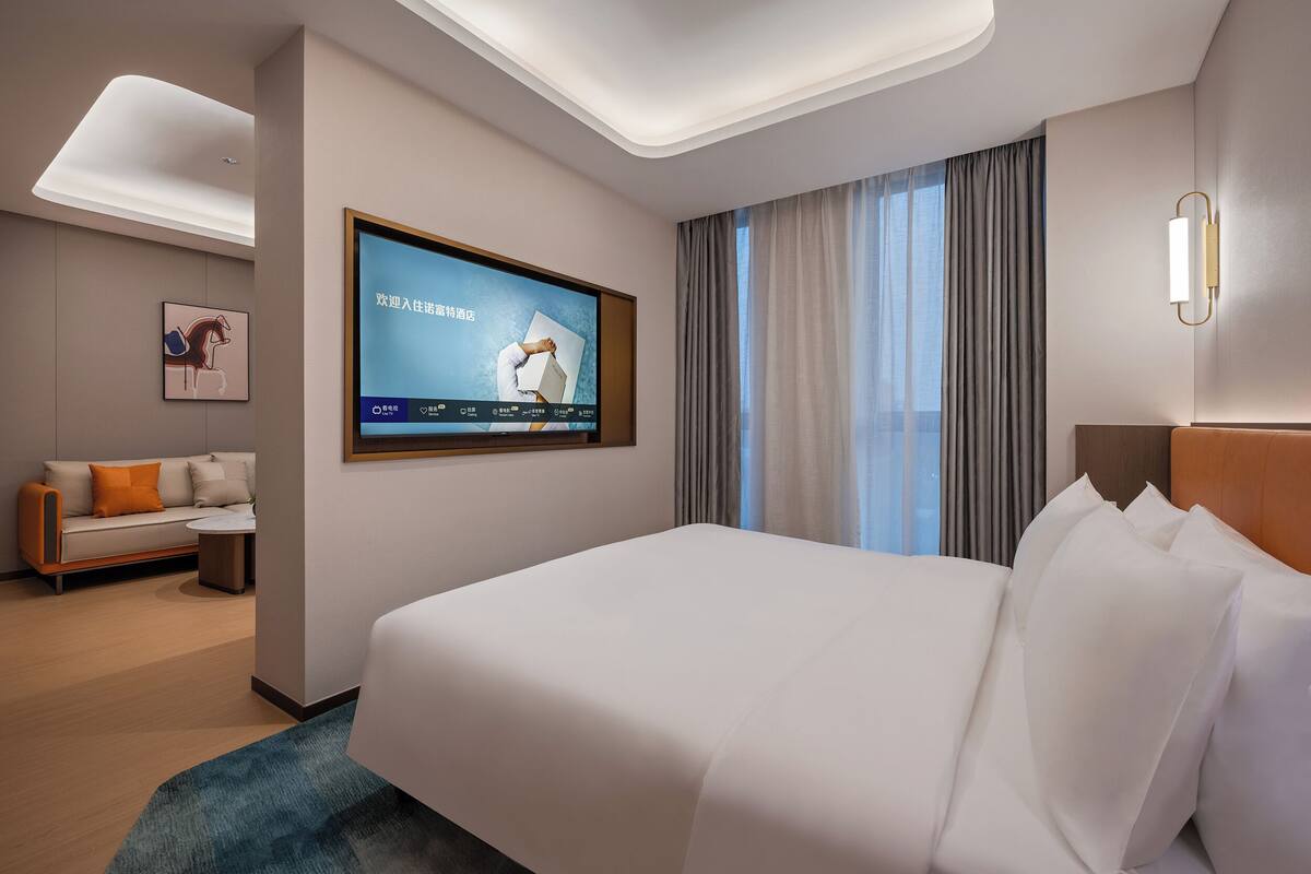 Une chambre d’hôtel moderne avec un grand lit, un téléviseur à écran plat fixé au mur, un canapé et une petite table.