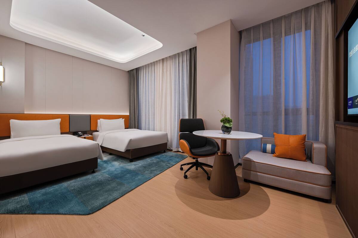 Une chambre d’hôtel moderne avec deux lits, un canapé, une petite table et un téléviseur.