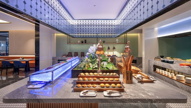 Un hall d’hôtel moderne avec un présentoir central où sont exposés des plats, un espace salon et un plafond décoratif.