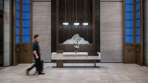 Un comptoir d’accueil avec un plateau en marbre, un vase rempli de fleurs et une sculpture fixée au mur.