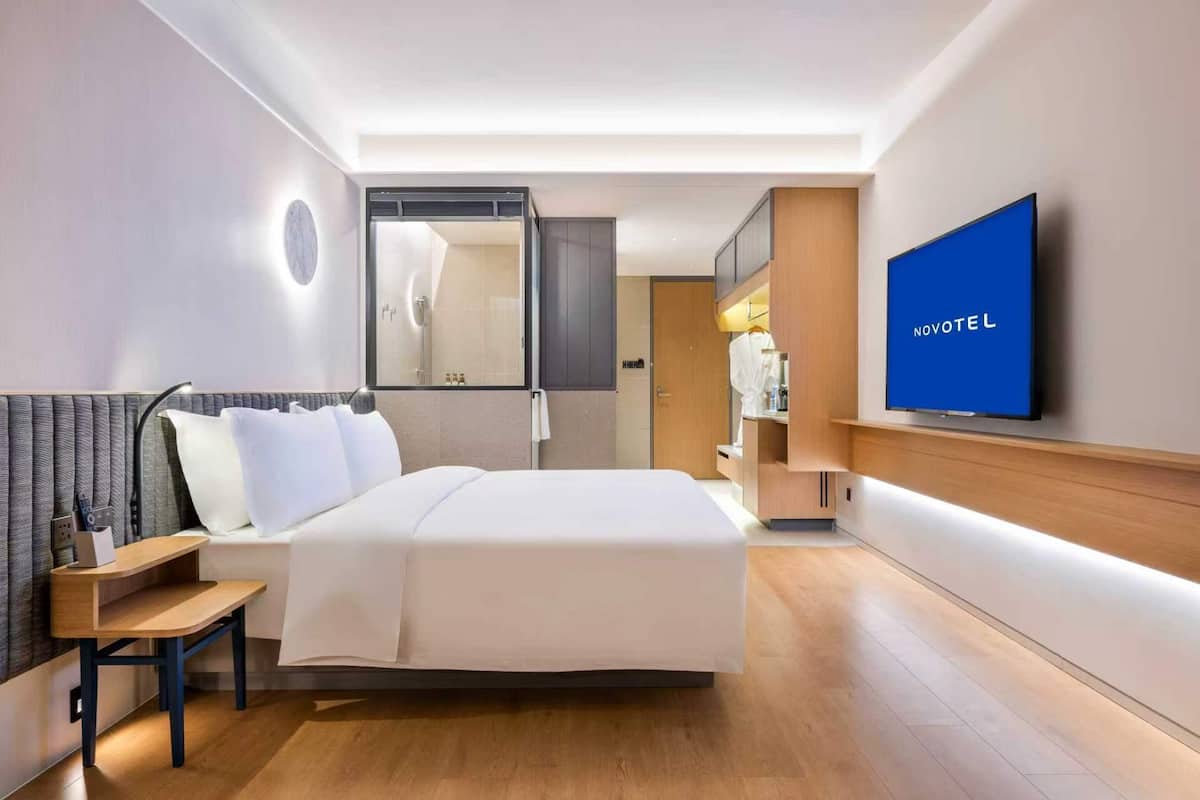 Een hotelkamer met een bed, nachtkastje, televisie en een spiegel.