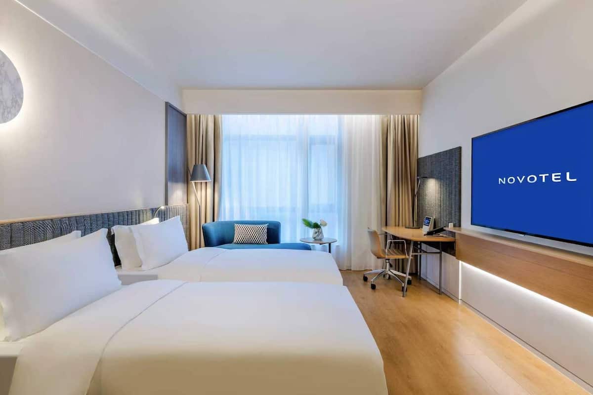 Een hotelkamer met twee bedden, een bureau, een televisie en een groot raam met gordijnen.