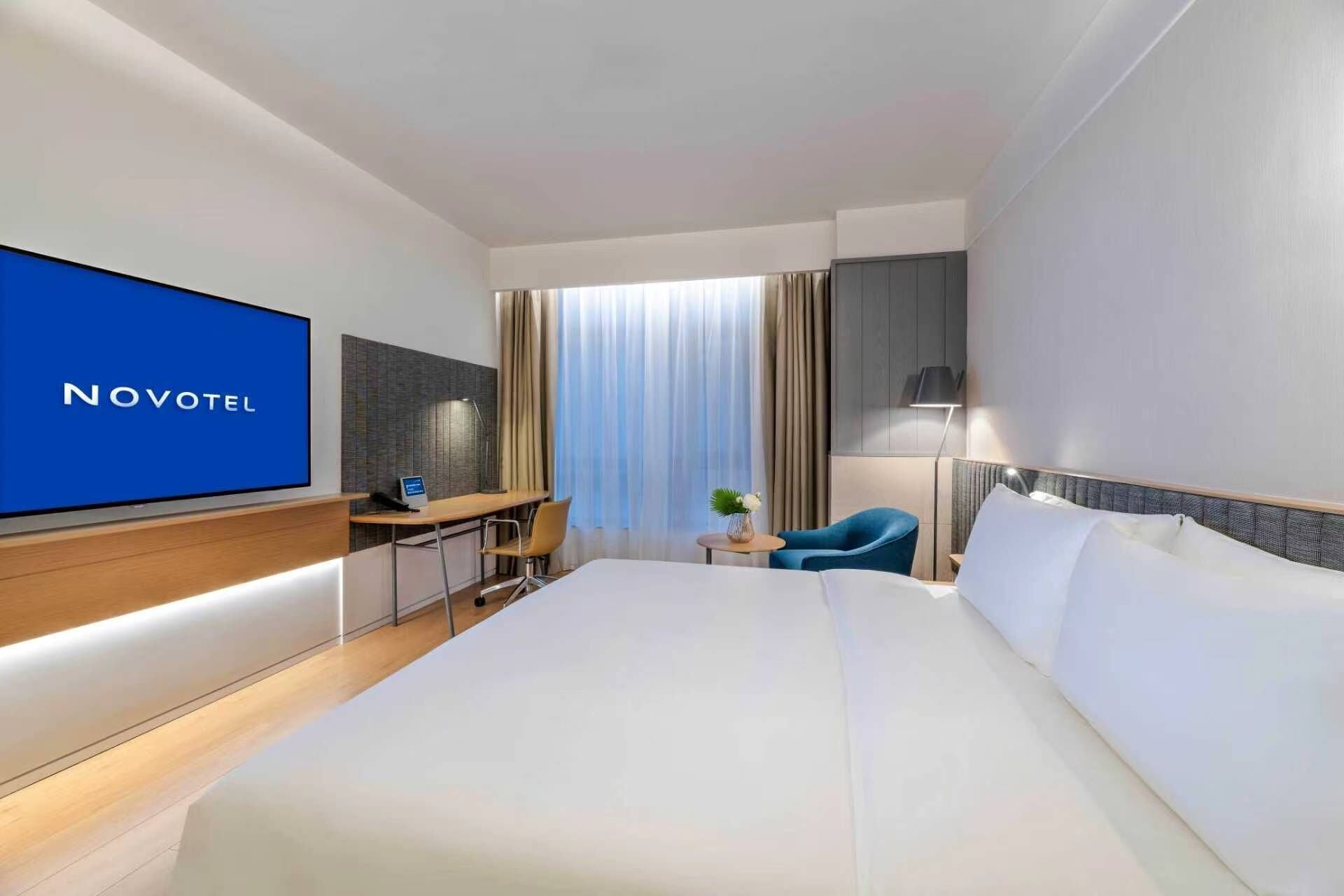 Ein Hotelzimmer mit Bett, Schreibtisch, Stuhl, Fernseher und einem Fenster mit Vorhängen.