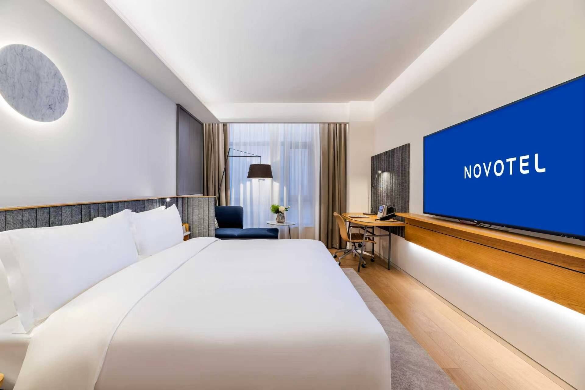A hotel room with a large bed, a desk with a chair, a television, and a view of the outdoors.
