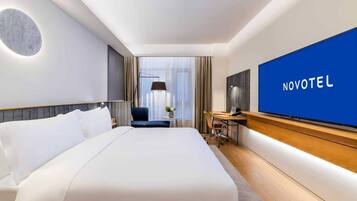Quarto de hotel com uma cama grande, uma escrivaninha com cadeira, televisão e vista para o exterior.