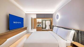 A hotel room with a bed, a TV, a robe, and a mirror.