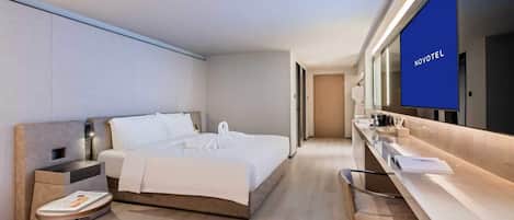 A modern hotel room with a bed, bedside table, chair, and a large mirror with a TV.