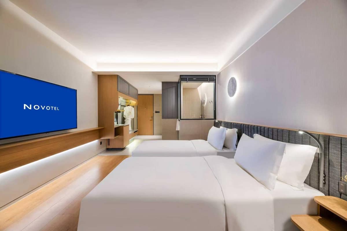 Een hotelkamer met een televisie, twee bedden, een garderobe en een spiegel.