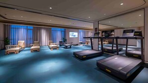 Ein Hotelzimmer mit einem großen Bett, einem Schreibtisch, einem Sessel und einem Laufband, sowie einem Fernsehbildschirm.