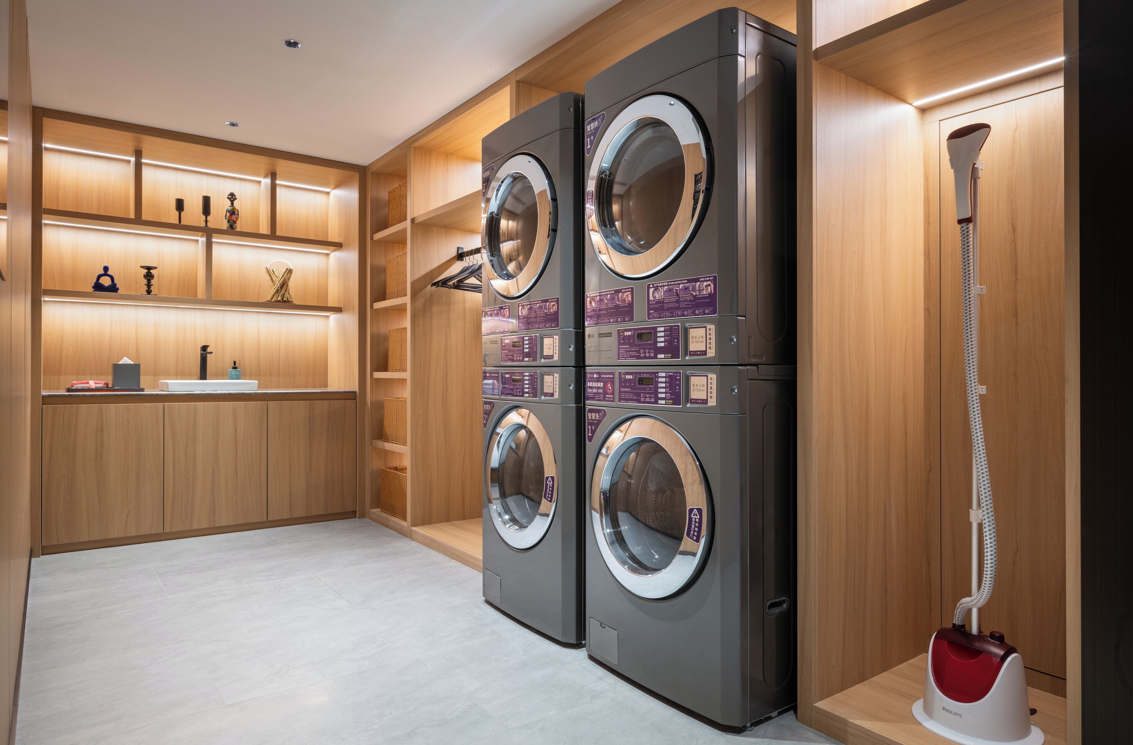 A modern laundry room with two front-loading washing machines, a built-in shelf with decorative items, and a vacuum cleaner.